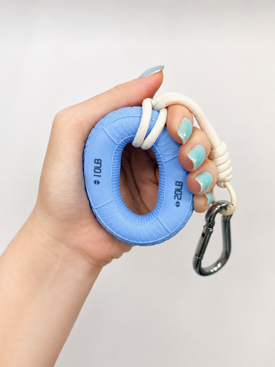 Boulder Grip Charm in light blue held in hand, showing climbing-inspired hand grip strengthener with carabiner