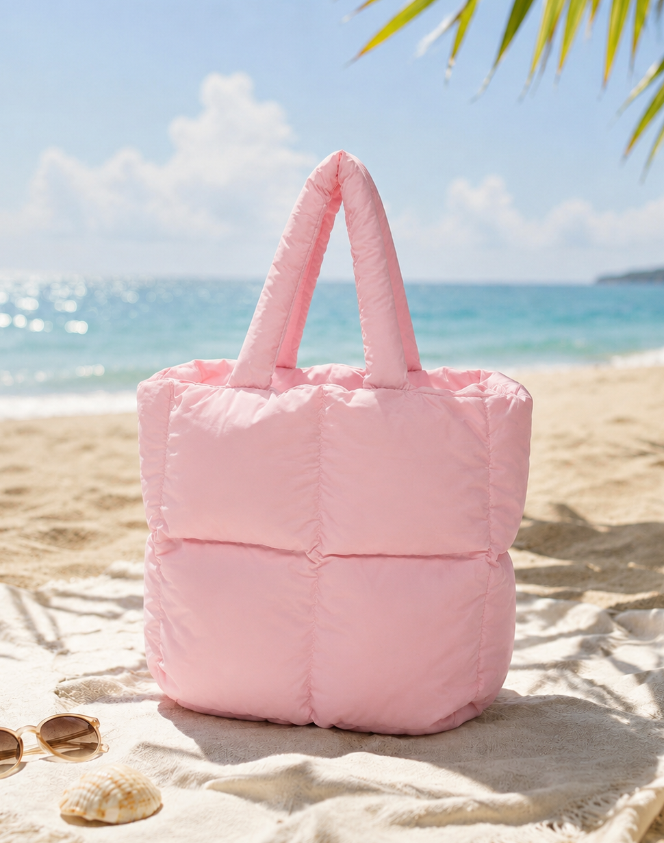 Mini Puffer Tote Bag in pink on sandy beach with sunglasses and seashells, ocean background