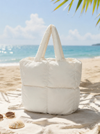 Mini Puffer Tote Bag in off-white on sandy beach with sunglasses and seashell, ocean and palm leaves background