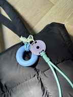 Boulder Grip Charm attached to a black puffer jacket, climbing-inspired bag charm in light blue and lavender